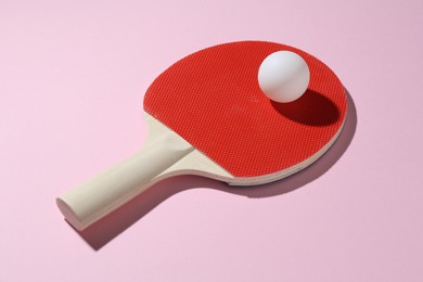 Photo of Ping pong racket and ball on pink background, closeup