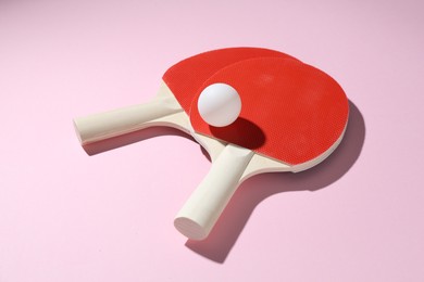Photo of Ping pong rackets and ball on pink background, closeup