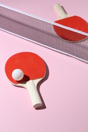 Photo of Ping pong rackets, ball and net on pink background, above view