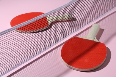 Photo of Ping pong rackets and net on pink background, closeup