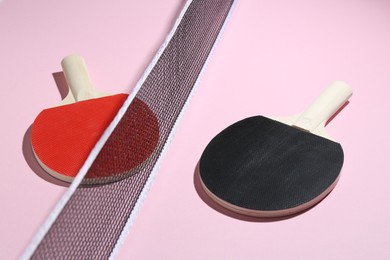 Photo of Ping pong rackets and net on pink background, closeup