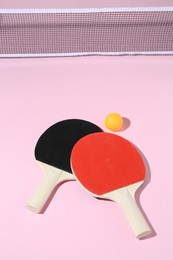 Photo of Ping pong rackets, ball and net on pink background, above view
