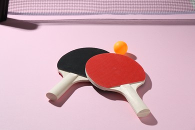 Photo of Ping pong rackets, ball and net on pink background, closeup