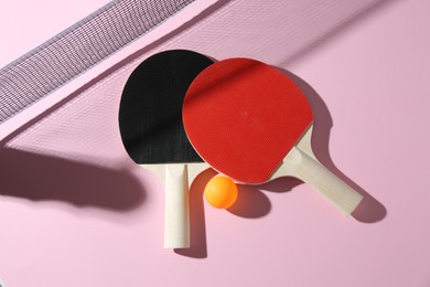 Photo of Ping pong rackets, ball and net on pink background, flat lay