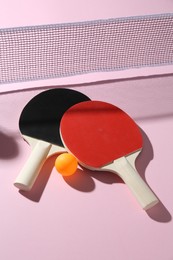 Photo of Ping pong rackets, ball and net on pink background, above view