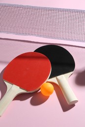 Photo of Ping pong rackets, ball and net on pink background, above view