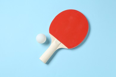 Photo of Ping pong racket and ball on light blue background, flat lay