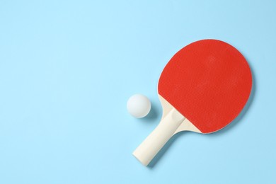 Photo of Ping pong racket and ball on light blue background, flat lay. Space for text