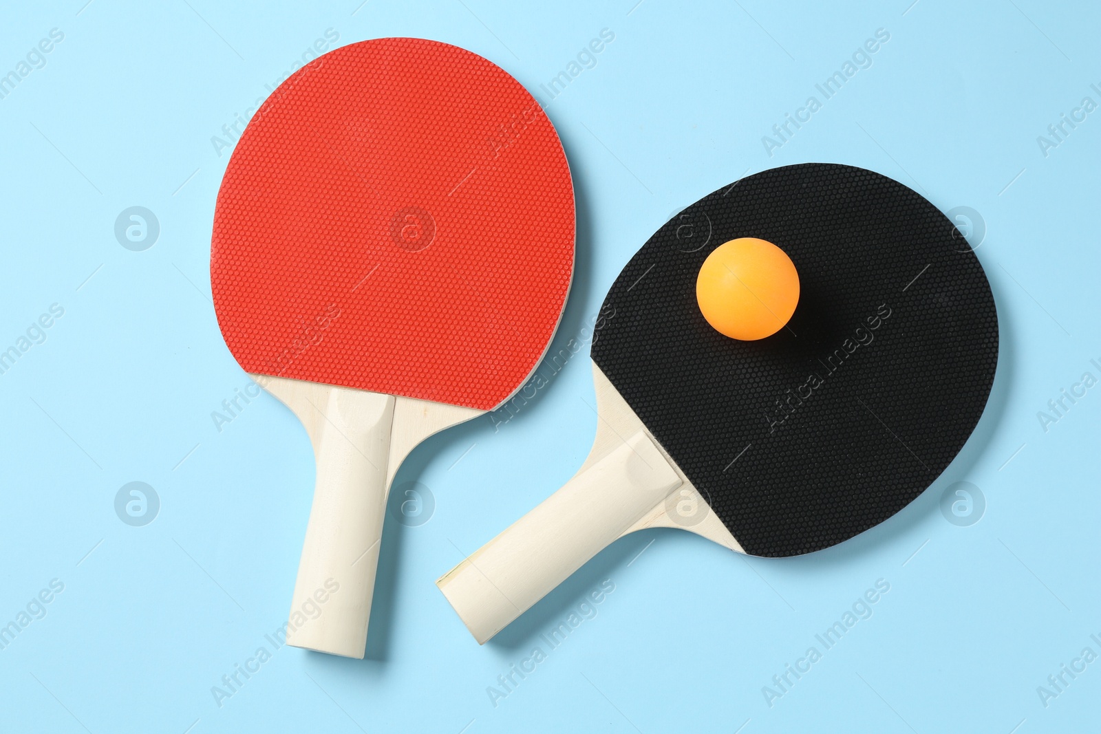 Ping pong rackets and ball on light blue background, flat lay Photo of Ping pong rackets and ball on light blue background, flat lay