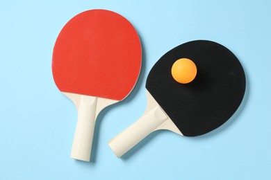 Photo of Ping pong rackets and ball on light blue background, flat lay
