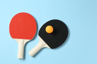 Photo of Ping pong rackets and ball on light blue background, flat lay. Space for text