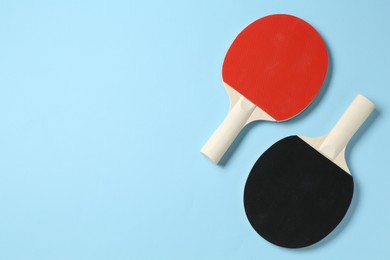 Photo of Ping pong rackets on light blue background, flat lay. Space for text