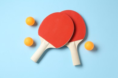 Photo of Ping pong rackets and balls on light blue background, flat lay