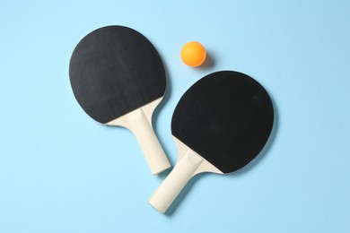 Photo of Ping pong rackets and ball on light blue background, flat lay