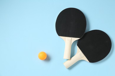 Photo of Ping pong rackets and ball on light blue background, flat lay. Space for text
