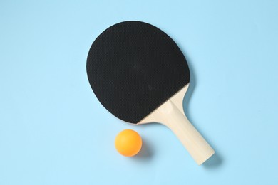 Photo of Ping pong racket and ball on light blue background, flat lay