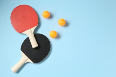 Photo of Ping pong rackets and balls on light blue background, flat lay. Space for text