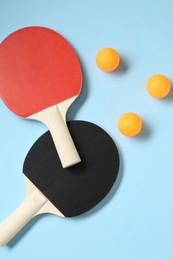 Photo of Ping pong rackets and balls on light blue background, flat lay