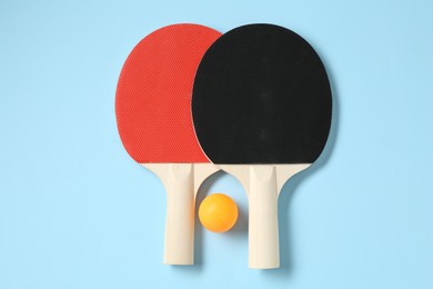 Photo of Ping pong rackets and ball on light blue background, flat lay