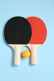 Photo of Ping pong rackets and ball on light blue background, flat lay