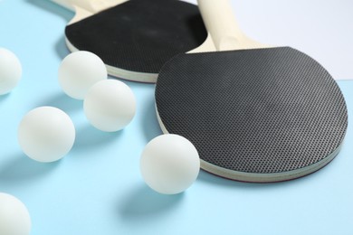 Photo of Ping pong rackets and balls on light blue background, closeup