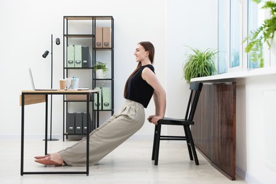 Photo of Beautiful woman exercising with chair in office