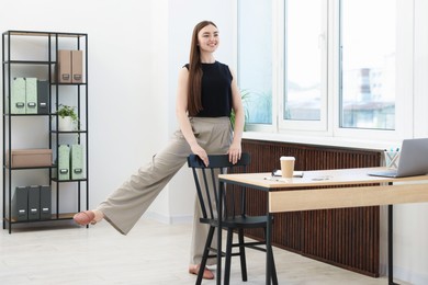 Photo of Beautiful woman exercising with chair in office