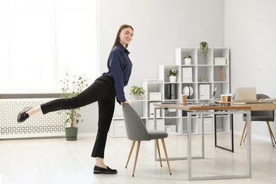 Photo of Beautiful woman exercising with chair in office