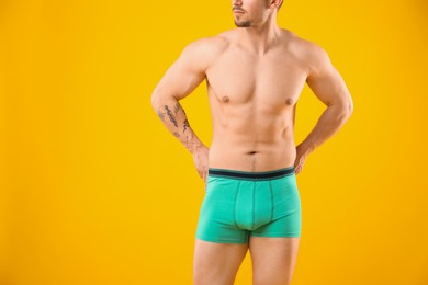 Photo of Young man in stylish turquoise underwear on orange background, closeup