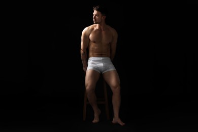 Photo of Young man in stylish white underwear on chair against black background