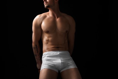 Photo of Young man in stylish white underwear on chair against black background, closeup
