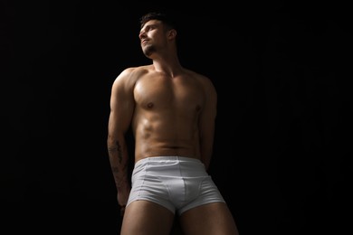 Photo of Young man in stylish white underwear on chair against black background, low angle view