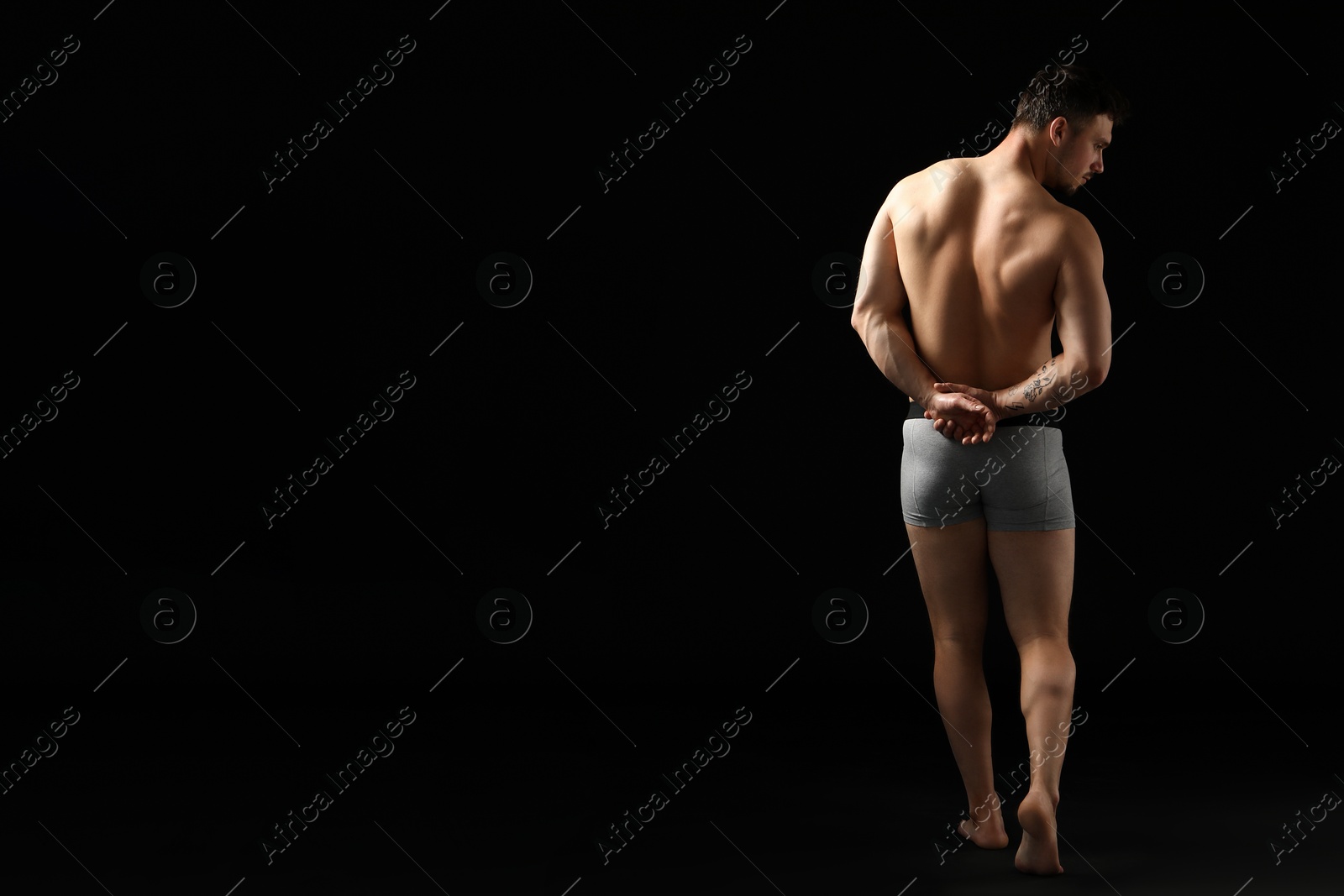 Young man in stylish light grey underwear on black background, back view. Space for text Photo of Young man in stylish light grey underwear on black background, back view. Space for text