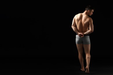 Photo of Young man in stylish light grey underwear on black background, back view. Space for text