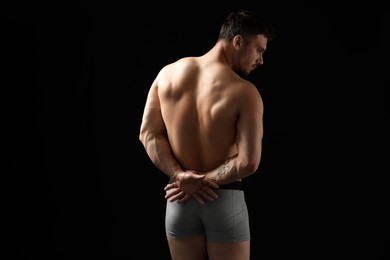 Photo of Young man in stylish light grey underwear on black background, back view