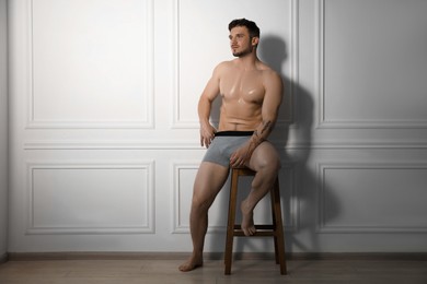 Photo of Young man in stylish light grey underwear on chair near white wall indoors