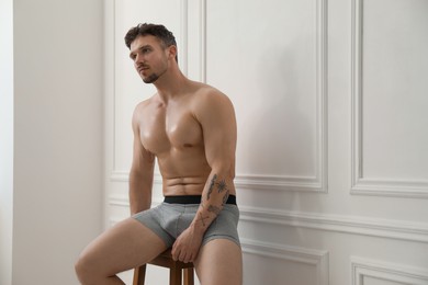 Photo of Young man in stylish light grey underwear on chair near white wall indoors. Space for text