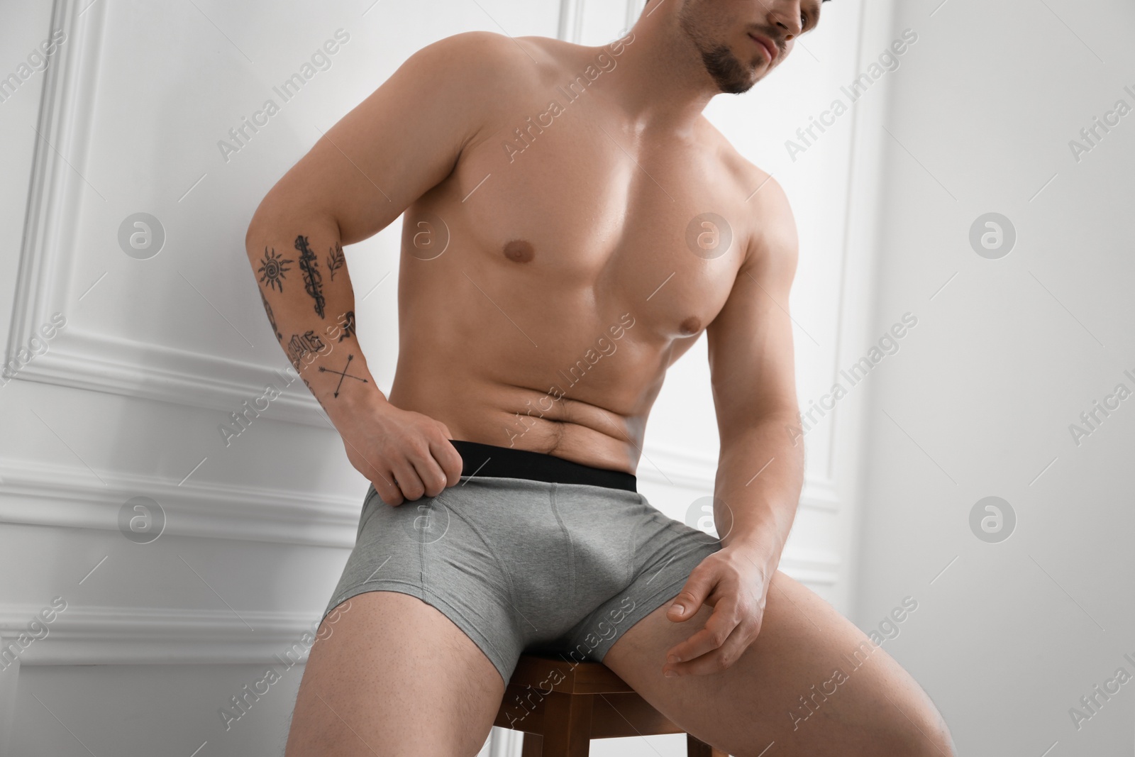 Young man in stylish light grey underwear on chair near white wall indoors, closeup Photo of Young man in stylish light grey underwear on chair near white wall indoors, closeup
