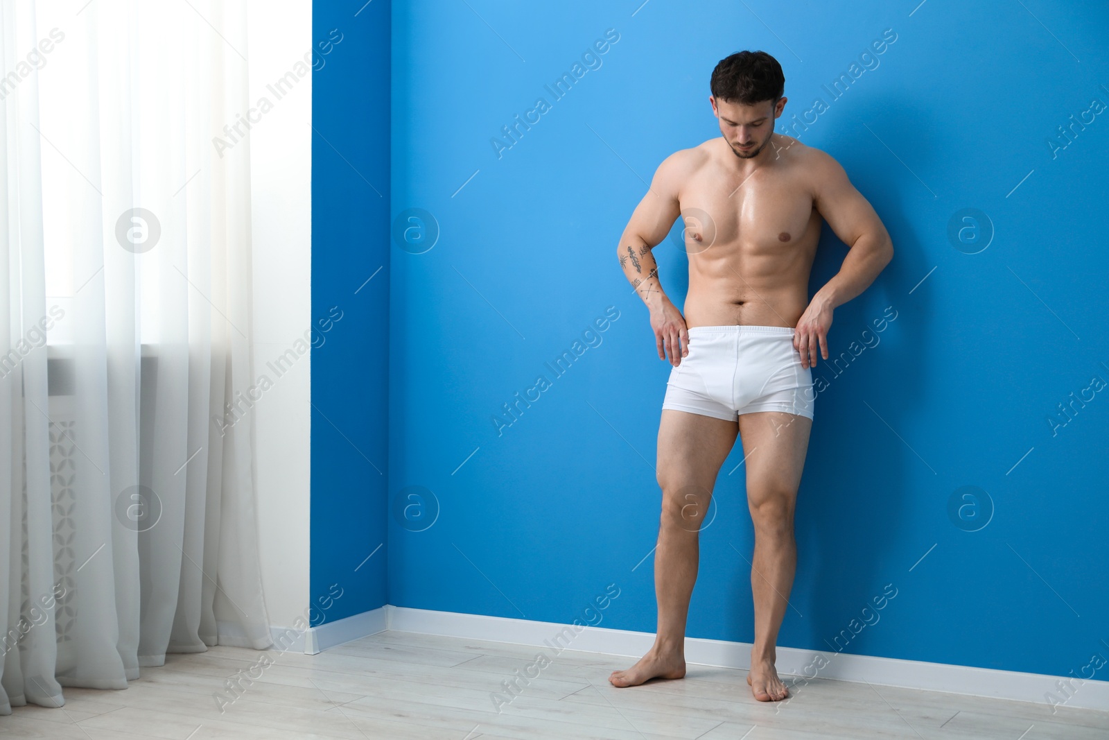 Young man in stylish white underwear near light blue wall indoors. Space for text Photo of Young man in stylish white underwear near light blue wall indoors. Space for text