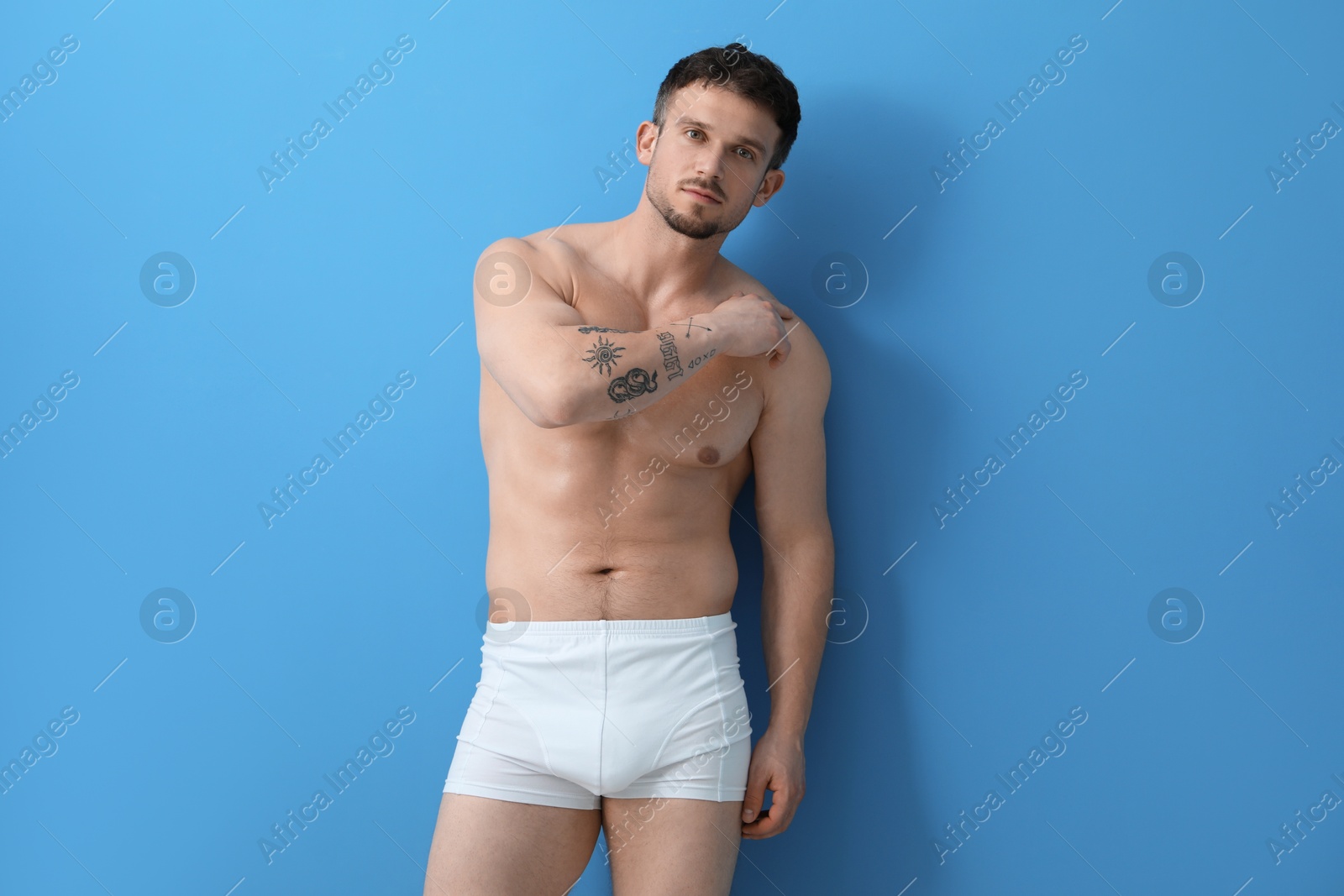 Young man in stylish white underwear on light blue background Photo of Young man in stylish white underwear on light blue background