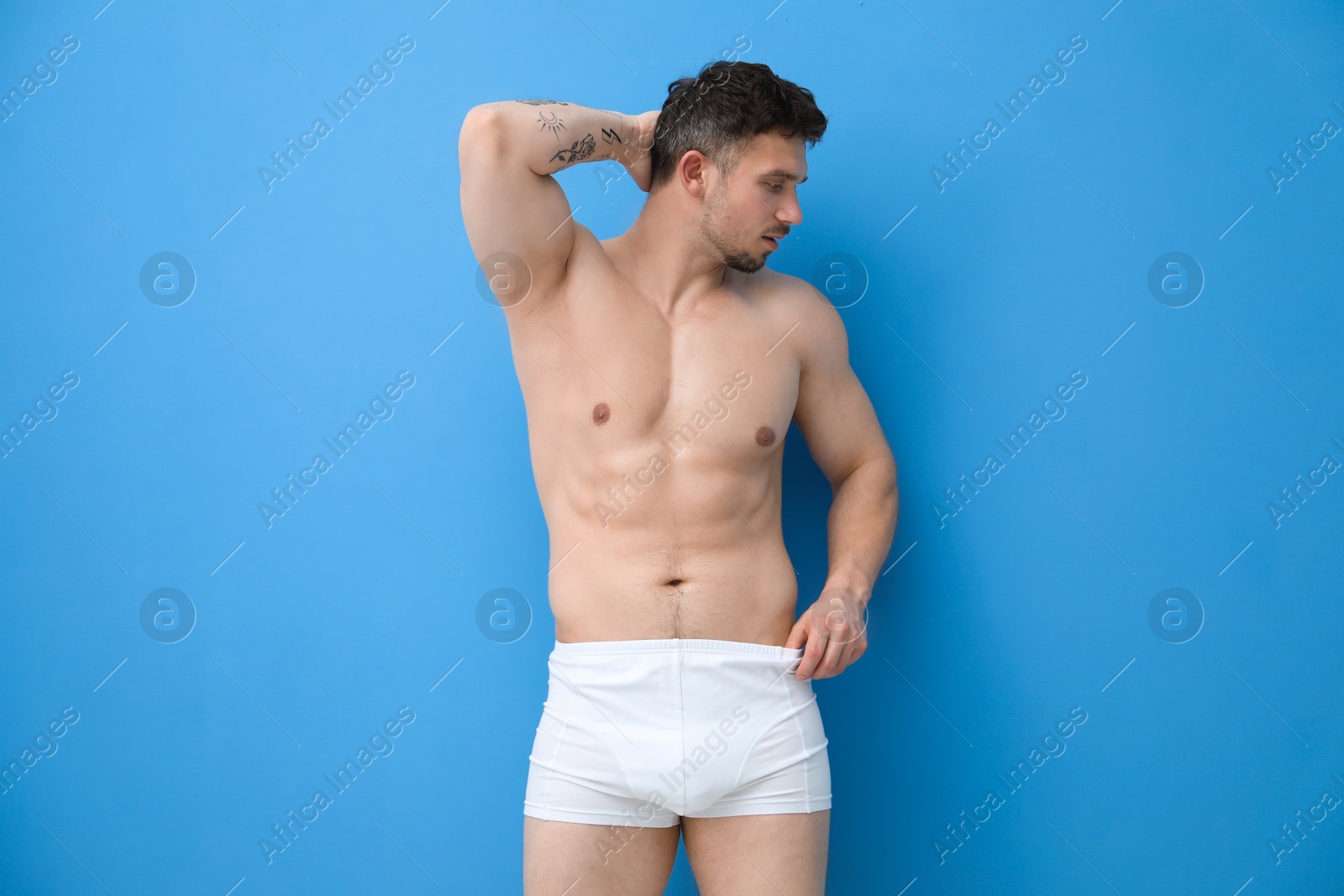 Young man in stylish white underwear on light blue background Photo of Young man in stylish white underwear on light blue background