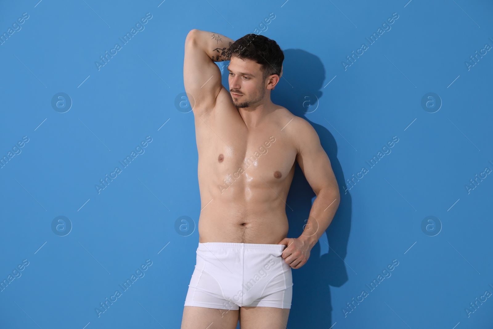 Young man in stylish white underwear on light blue background Photo of Young man in stylish white underwear on light blue background