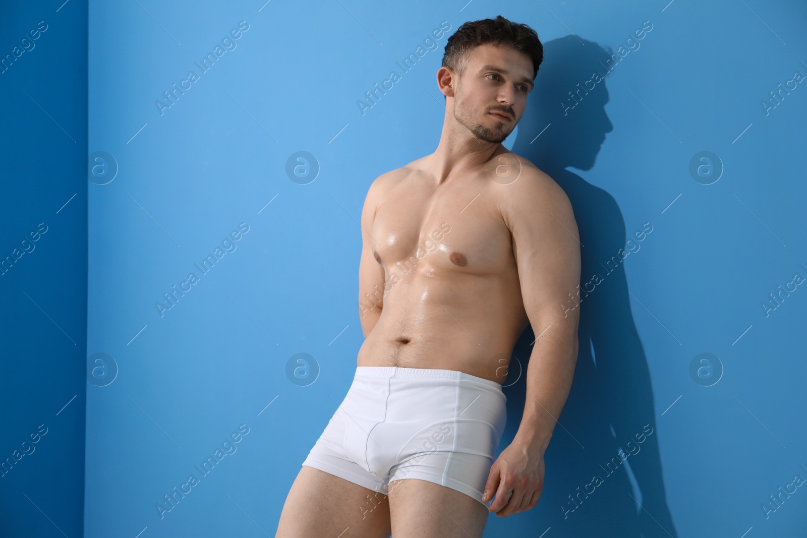 Young man in stylish white underwear near light blue wall indoors Photo of Young man in stylish white underwear near light blue wall indoors