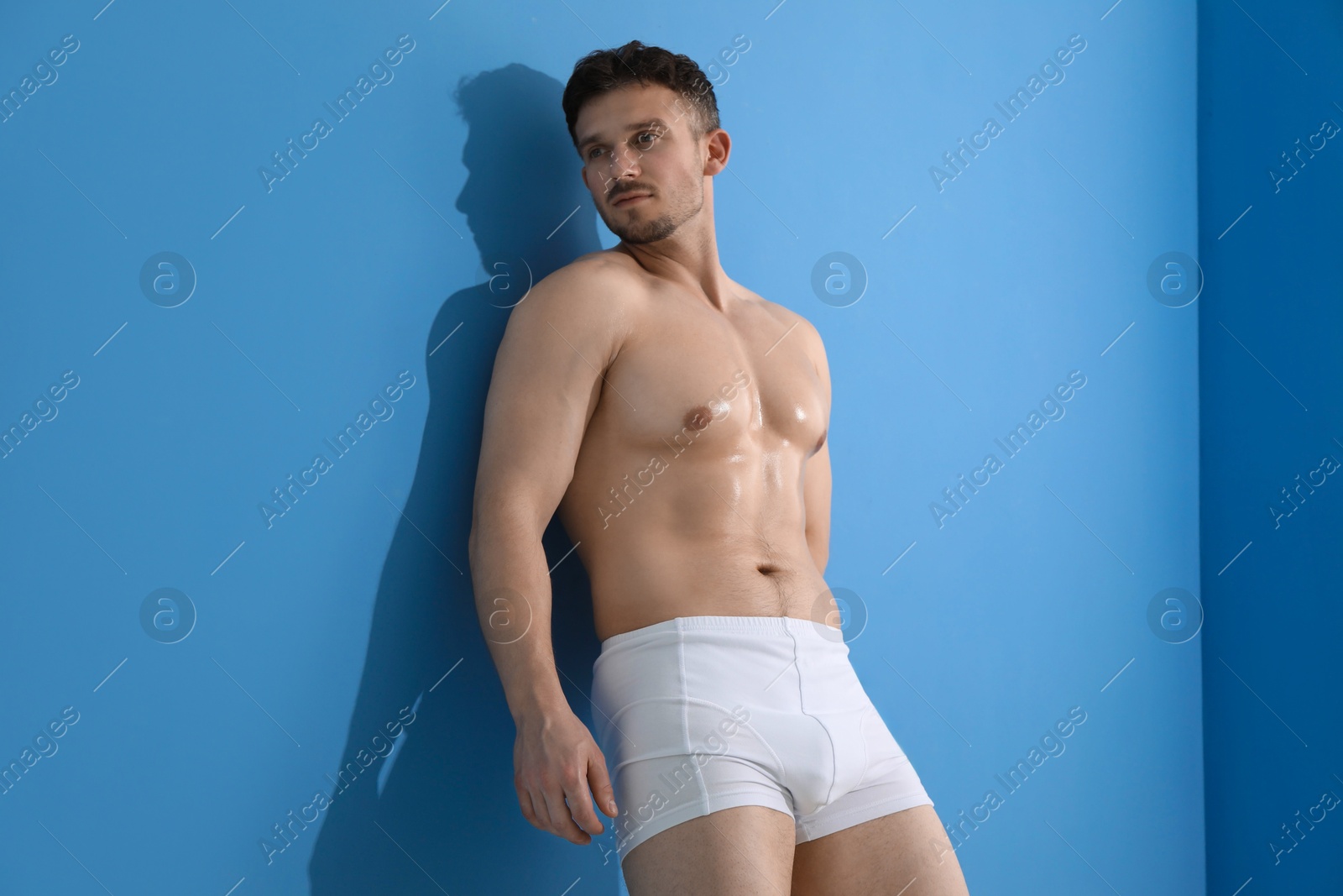 Young man in stylish white underwear near light blue wall indoors Photo of Young man in stylish white underwear near light blue wall indoors