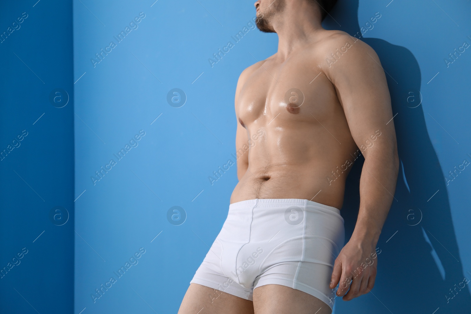 Young man in stylish white underwear near light blue wall indoors, closeup. Space for text Photo of Young man in stylish white underwear near light blue wall indoors, closeup. Space for text