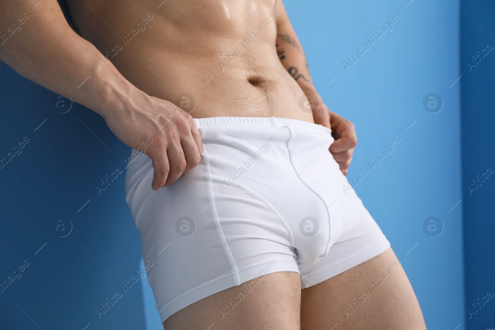 Young man in stylish white underwear near light blue wall indoors, closeup Photo of Young man in stylish white underwear near light blue wall indoors, closeup
