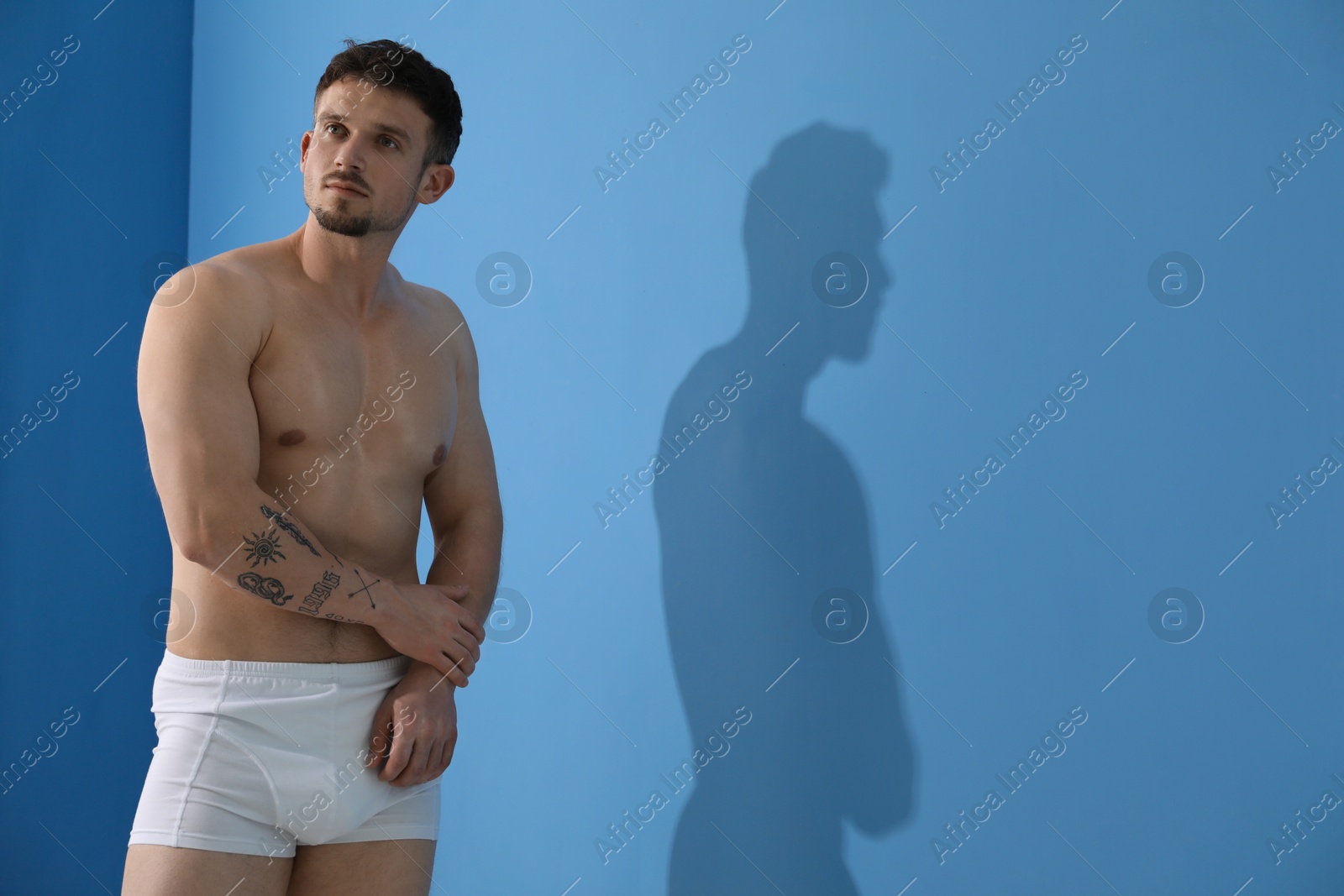 Young man in stylish white underwear near light blue wall indoors. Space for text Photo of Young man in stylish white underwear near light blue wall indoors. Space for text