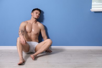 Photo of Young man in stylish white underwear near light blue wall indoors. Space for text