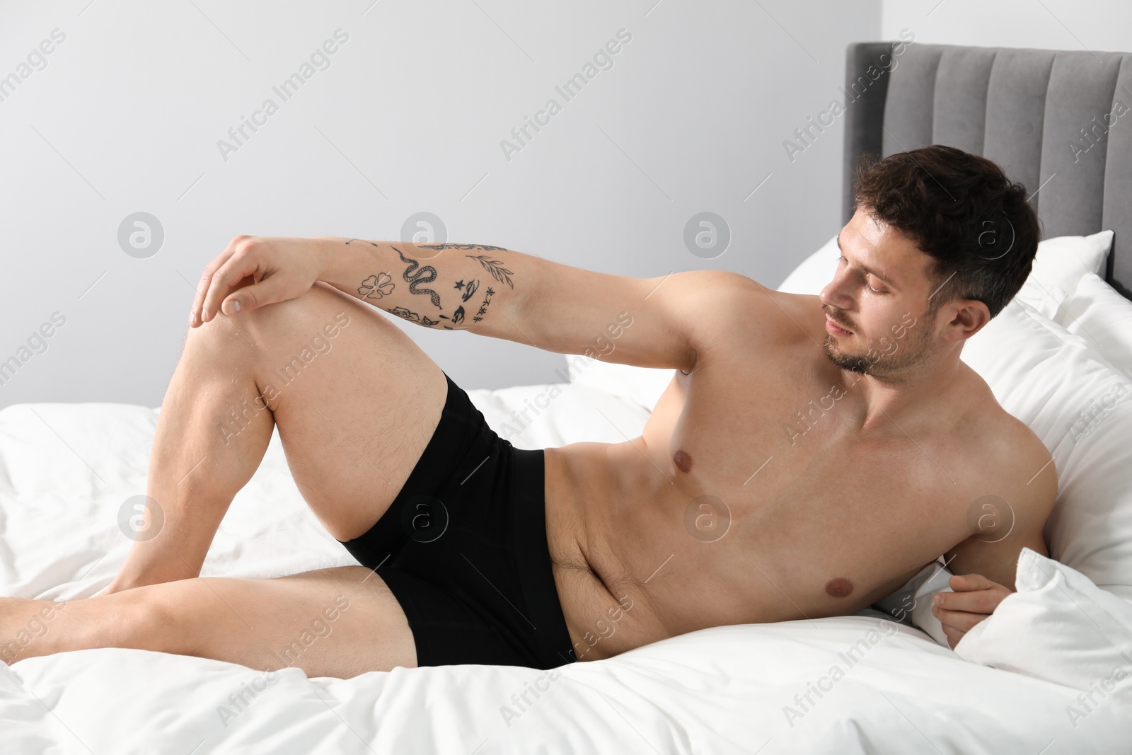 Young man in stylish black underwear on bed indoors Photo of Young man in stylish black underwear on bed indoors