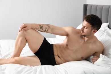 Photo of Young man in stylish black underwear on bed indoors
